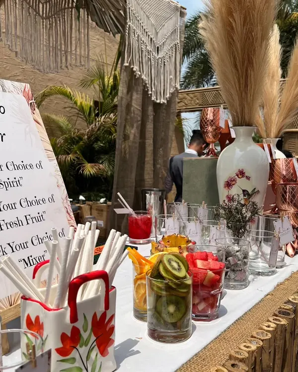Our interactive DIY Mojito Bar is a highlight of this boho setup. It features a bamboo-lined counter, macrame hangings, and fresh fruit for guests to create their own cocktails.