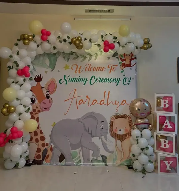 A cute jungle animal theme for a naming ceremony. The backdrop features a giraffe, elephant, and lion, framed by a balloon arch and complemented by "BABY" blocks for a complete photo-ready setup.