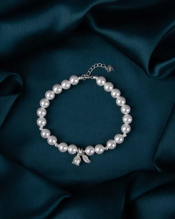 A delicate silver and pearl bracelet, shot on a dark teal satin background to create a feeling of elegance and luxury.