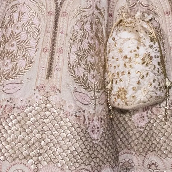 A close-up of the intricate floral and lattice embroidery on our ivory bridal lehenga. The matching potli bag also features the same detailed craftsmanship.