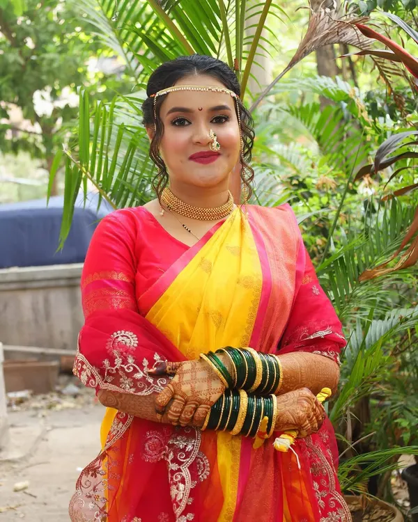 A classic Maharashtrian bride in a vibrant yellow and red saree. Her makeup is traditionally elegant with a focus on defined eyes, a small bindi, and a radiant complexion.