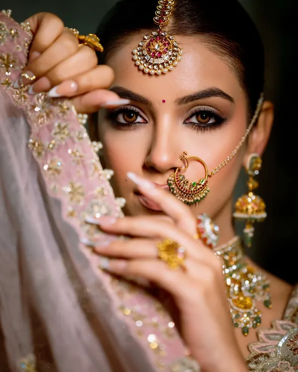 This is the kind of intense, dreamy look I love to create. The focus here is on the dramatic smoky eyes, defined brows, and flawless skin, all framed by traditional jewelry like the nath and maang tikka. It’s a perfect example of balancing bold details with overall elegance for a bridal portrait.