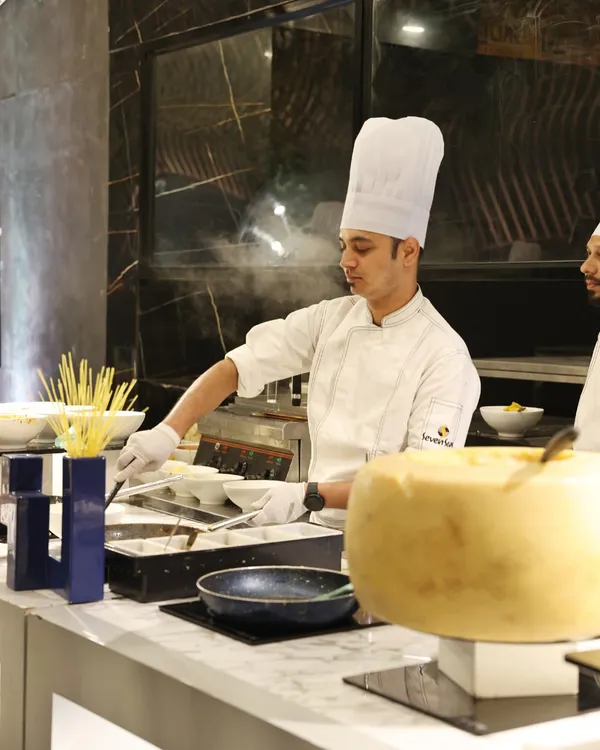 The magic of fresh pasta being prepared at our "Al Dente" live station. A chef tosses spaghetti in a pan, with a large wheel of Parmesan cheese ready for the final touch, creating an authentic Italian experience.