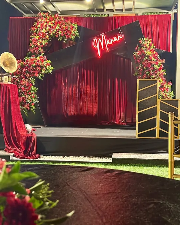 A glamorous stage setup for a musical night. The decor featured a custom neon sign with the host's name, a rich red velvet backdrop, and dramatic floral arrangements.