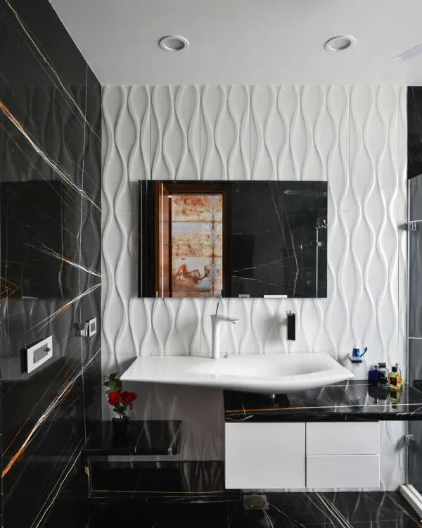 This bathroom in the Gupta Residence combines luxury and modernity with bold contrasts. Black tiles with golden veins define the space, while 3D white textured tiles add depth behind the minimalist vanity.