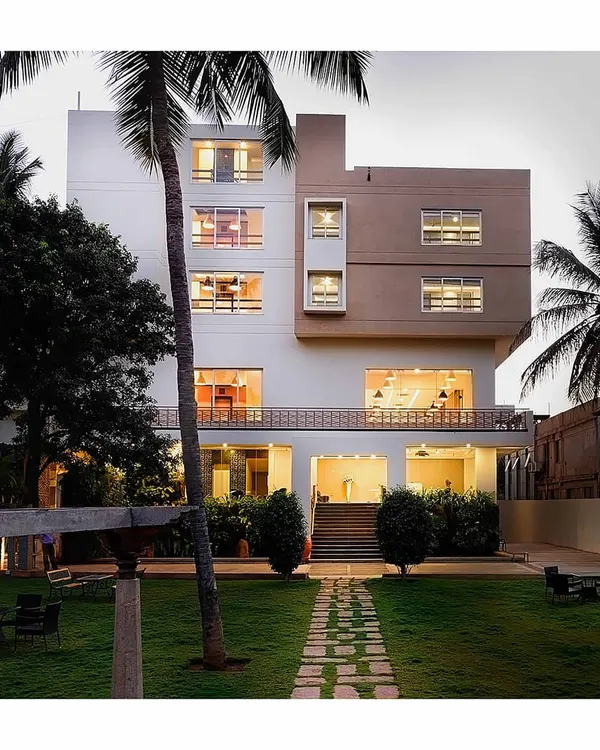 The entrance to this hotel is defined by a classic and elegant landscape design. A manicured lawn, flanked by tall palm trees and a central stone pathway, creates an inviting and upscale welcome for guests.