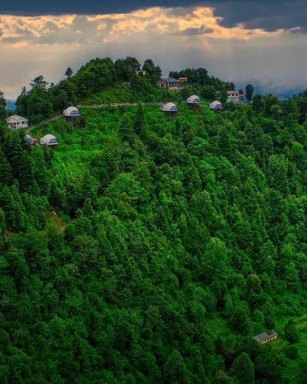 A breathtaking aerial view of Keekoo Stays in Kanatal, nestled amidst a lush green forest. This shot captures the scale and seclusion of the property, highlighting the dome stays as a unique hillside adventure.