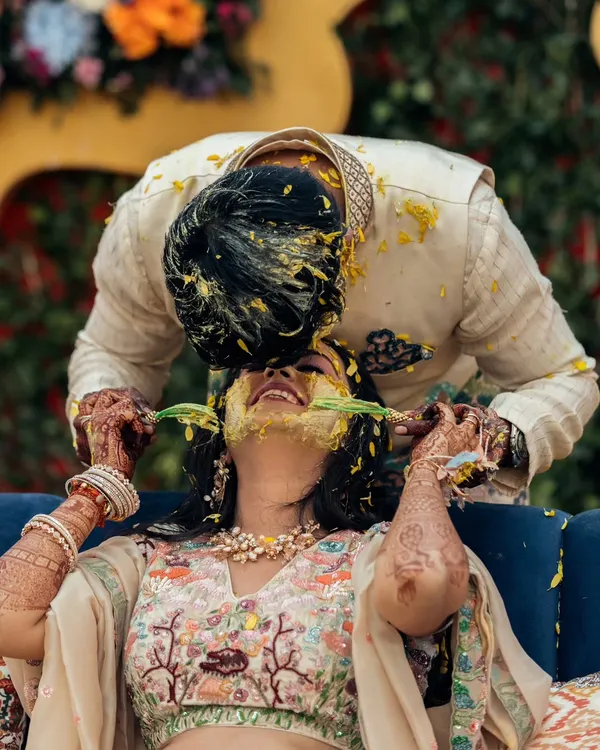 A playful and candid moment where the groom lovingly applies haldi to the bride's face. Their laughter and intimacy make this a standout shot from the pre-wedding festivities.