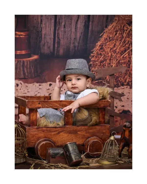 This dapper little boy tips his hat, adding a touch of old-school charm to his vintage photoshoot. The rustic barn backdrop and wooden cart create a timeless, classic feel.