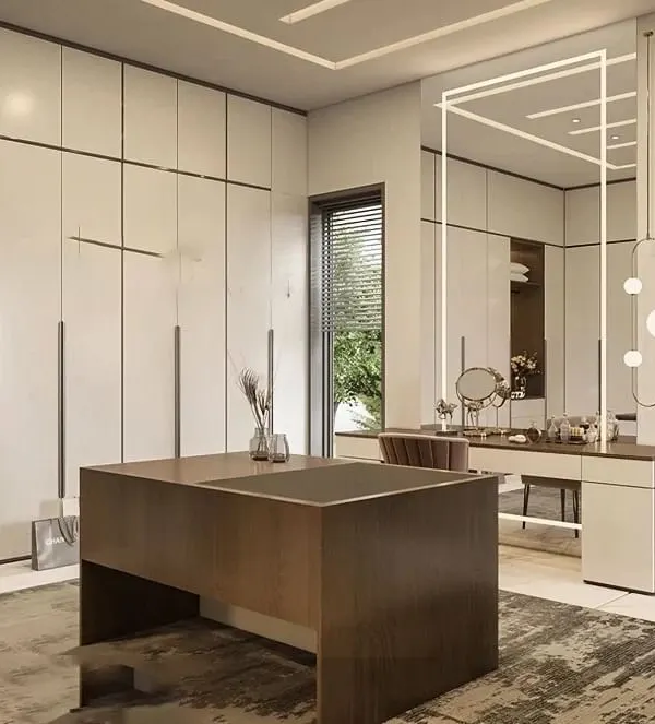 A sophisticated walk-in closet and dressing room featuring floor-to-ceiling off-white wardrobes, a central island with drawers, and a dedicated vanity table with statement lighting. This design creates a luxurious and organized personal space.