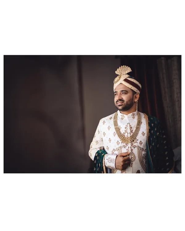 A quiet moment of preparation for the groom. This portrait captures him looking thoughtful and handsome in his wedding sherwani just before the ceremony begins.