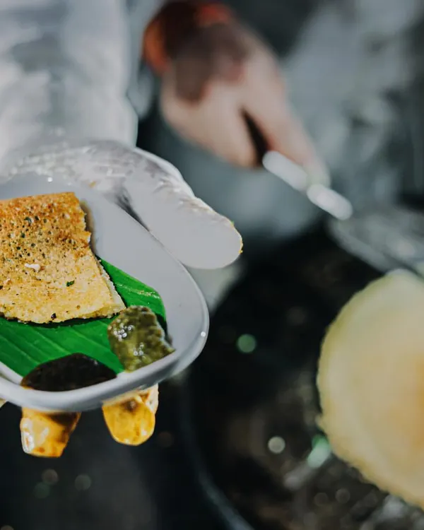 The sizzle of a fresh dosa being made is a highlight at any event. A chef serves a mini dosa on a banana leaf, offering a bite-sized piece of South Indian culinary art.