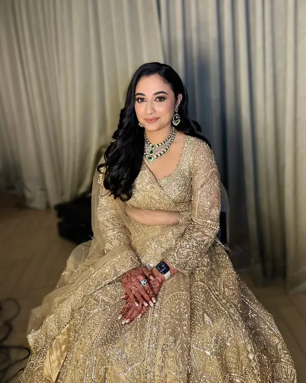 A full-length shot of my beautiful reception bride, Neha. She looks absolutely regal in her golden lehenga, with makeup that features soft golden eyes and a flawless base, complemented by elegant side-swept waves.