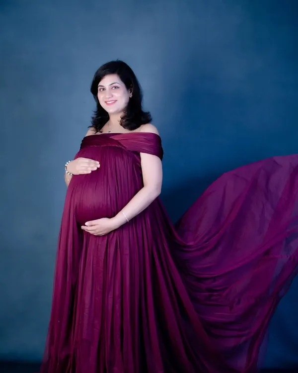 The magic of a fabric toss. This off-the-shoulder maternity gown in a rich magenta color creates a beautiful, dynamic shape, making for a truly show-stopping portrait.