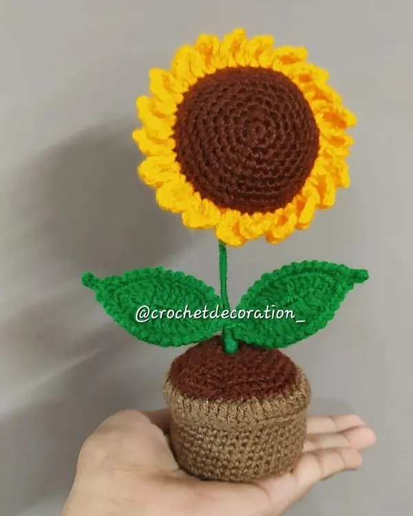 Our standard-sized crochet sunflower in a pot, held to show its scale. This piece is perfect for a desk or shelf, adding a touch of handmade sunshine to your decor.