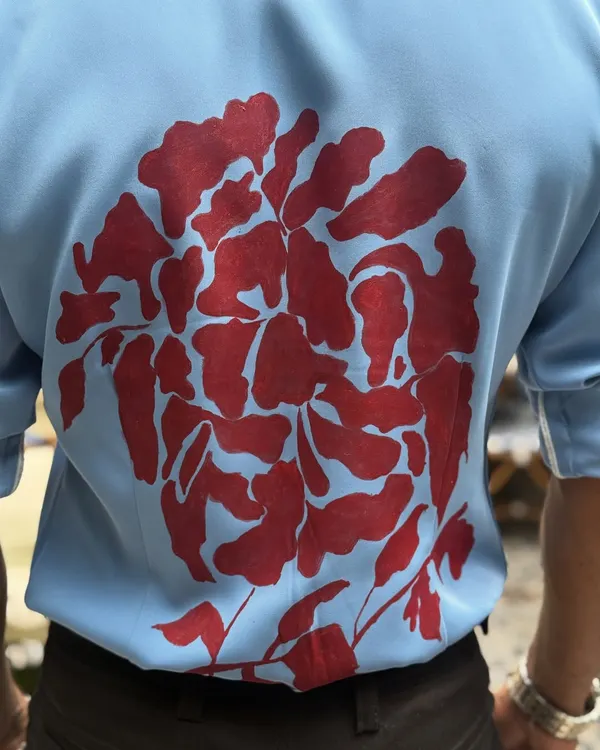 A close-up of the intricate hand-painted design on the back of our light blue shirt. This showcases the unique artistry and craftsmanship that goes into our one-of-a-kind pieces.