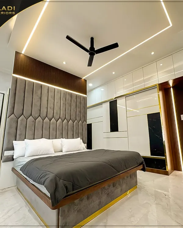 A luxurious master bedroom featuring a floor-to-ceiling grey upholstered headboard with geometric patterns. The design is enhanced by gold trim details on the bed and wardrobe, creating a cohesive and opulent look.