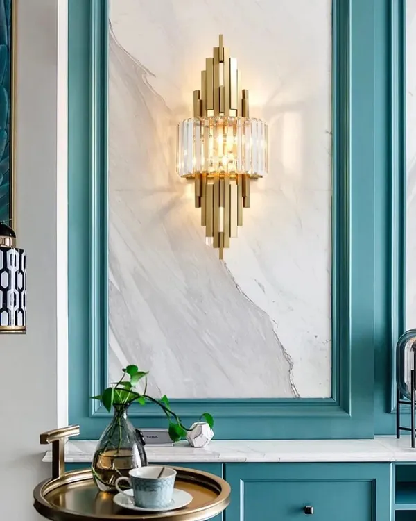 This Art Deco inspired wall sconce is a true masterpiece, combining geometric gold metalwork with brilliant crystal. It is designed to be a focal point, casting intricate patterns of light and shadow to elevate a living room or entryway.
