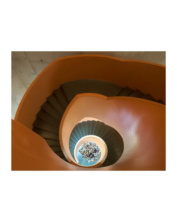 An overhead view looking down a vibrant orange spiral staircase. This image captures how a staircase can become a powerful formal element, using geometry and color to create a dynamic spatial experience.
