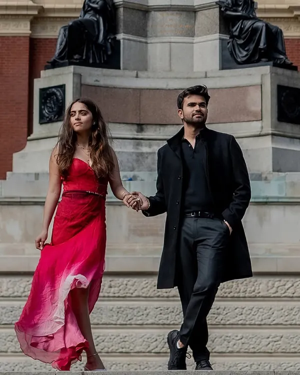 A powerful, fashion-forward portrait on the steps of the Royal Albert Hall in London. The bride's flowing red dress and the couple's confident pose create a striking image of modern romance.