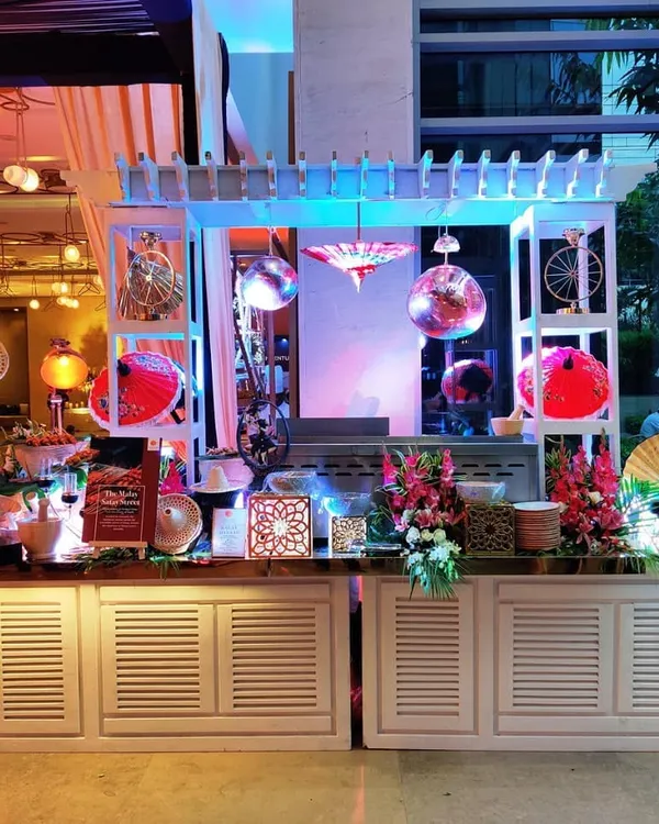 A whimsical and colorful Asian-themed food station designed for a corporate event at Hotel Andaz, New Delhi. The setup features decorative fans, umbrellas, and disco balls, creating a fun and memorable ambiance.