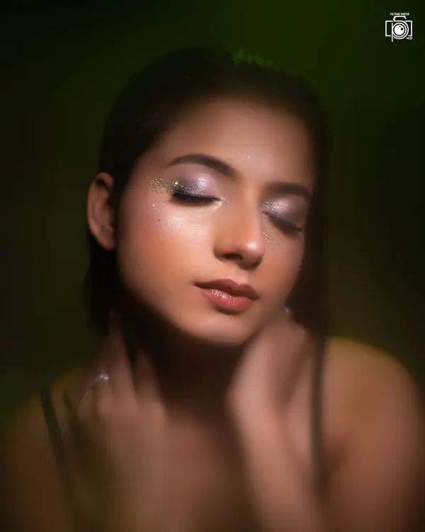 A dreamy beauty portrait with eyes closed to showcase the sparkling glitter eyeshadow. The soft, diffused lighting with a hint of green creates an ethereal and magical mood.