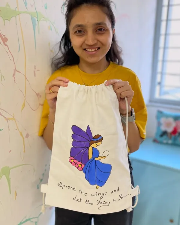A participant proudly displays the fairy-themed backpack she painted in our workshop. It's a perfect way to express your personal style.