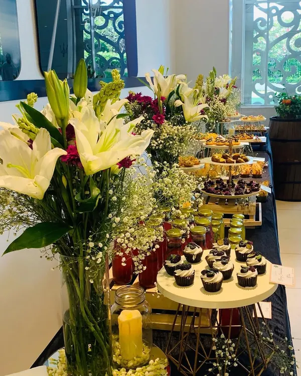 For a sophisticated event, I arranged this beautiful dessert and drinks table. The setup includes tall glass vases with fresh lilies and other flowers, adding a touch of elegance to the culinary display.