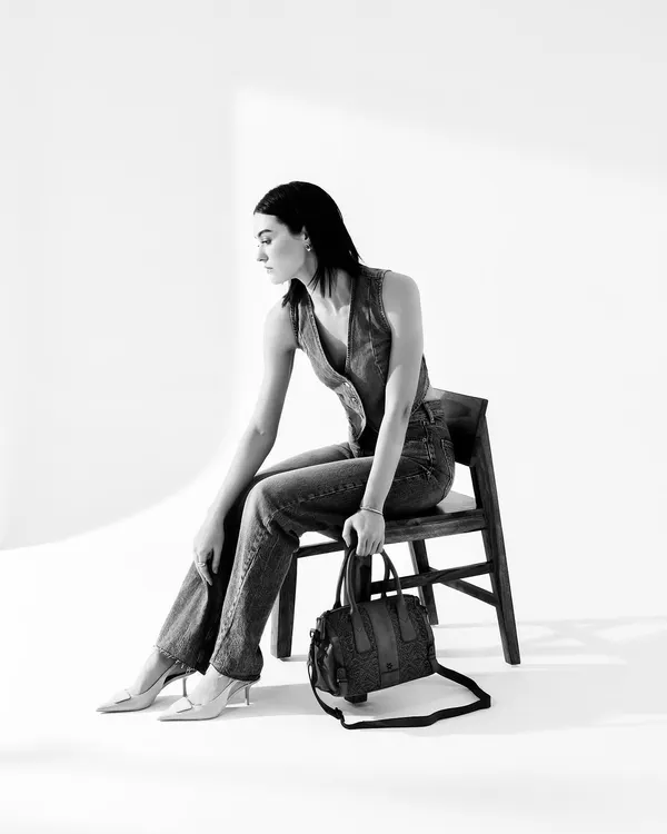 A minimalist black and white studio shot for Kompanero's Autumn/Winter campaign. The clean background and classic styling put the focus entirely on the model's silhouette and the handbag's design.