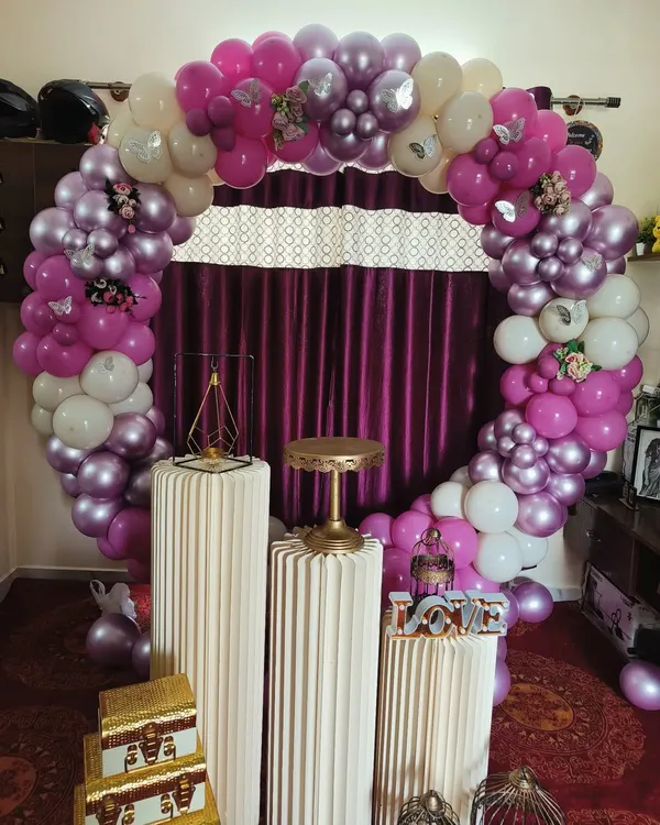 This full circular balloon arch in shades of purple, pink, and white creates a beautiful frame for your cake-cutting ceremony. The setup is completed with elegant white pedestals and decorative props for a cohesive look.