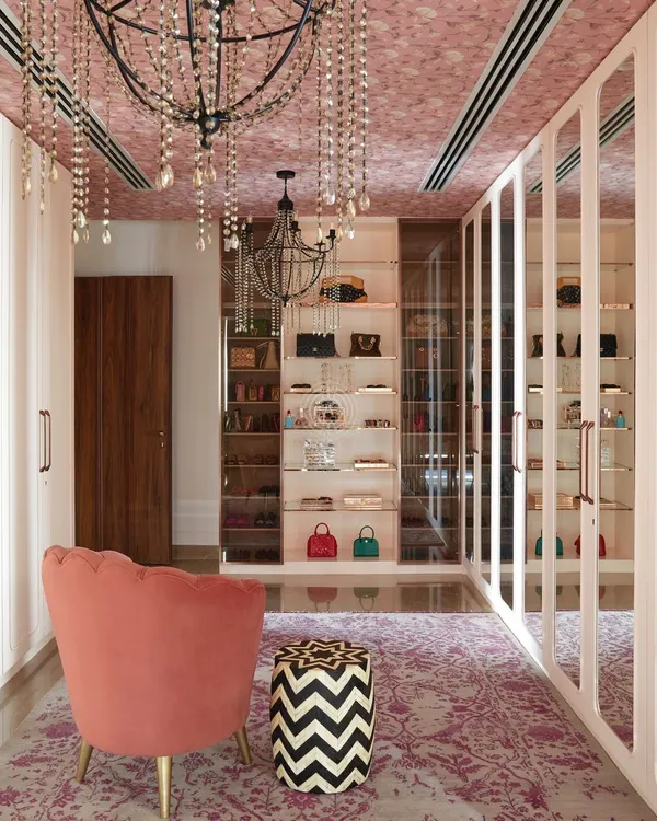 This walk-in wardrobe from our 'Palace in the Sky' project is pure luxury. We used soft pink hues, a wallpapered ceiling with crystal chandeliers, and custom shelving to display a stunning bag collection.