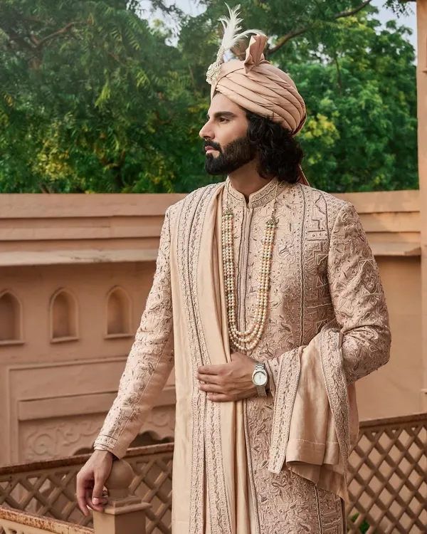 For the modern groom who honors tradition, I present this regal sherwani in a subtle pastel hue. The complete ensemble, from the feathered safa to the layered pearl necklace and the intricately embroidered stole, is designed to create a timeless and majestic wedding day look.