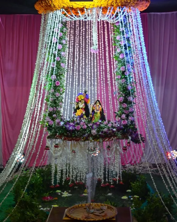 A divine swing setup for Radha and Krishna, decorated with an arch of fresh flowers and cascading strings of rajnigandha. The lighting adds a magical touch, making it a beautiful centerpiece for Janmashtami puja.