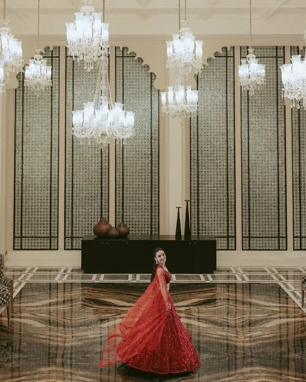 A breathtaking wide-angle portrait of the bride in a magnificent hall. The sweeping red lehenga, the grand chandeliers, and the opulent decor all combine to create a truly regal image.