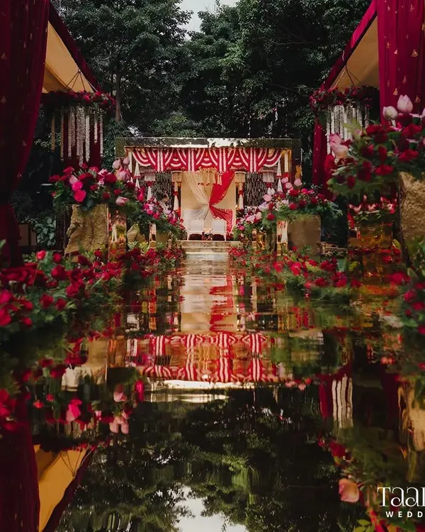 The centerpiece of this South Indian decor was the stunning mirror glass aisle. It created a breathtaking reflection of the sky, the lush greenery, and the vibrant red floral arrangements, making the bride's walk feel like a journey through a floral wonderland.