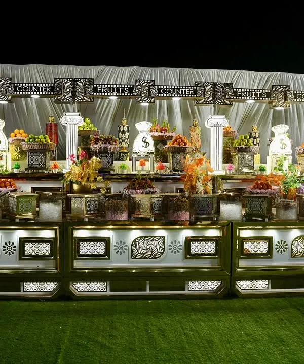 A lavish and beautifully lit dessert and fruit buffet. The symmetrical arrangement and ornate white and gold counter create a stunning display that invites guests to indulge.