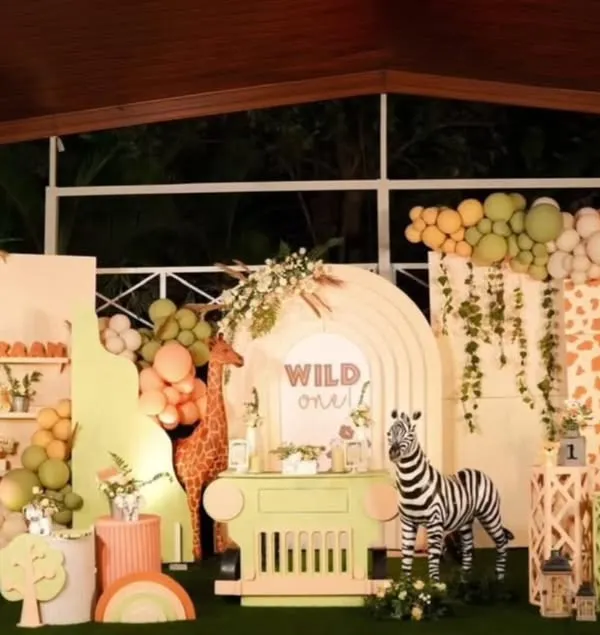 A grand "Wild One" jungle safari theme for a first birthday. This full-stage decoration includes multiple backdrops, custom arches, a dessert cart, and life-sized animal props like a zebra and elephant.