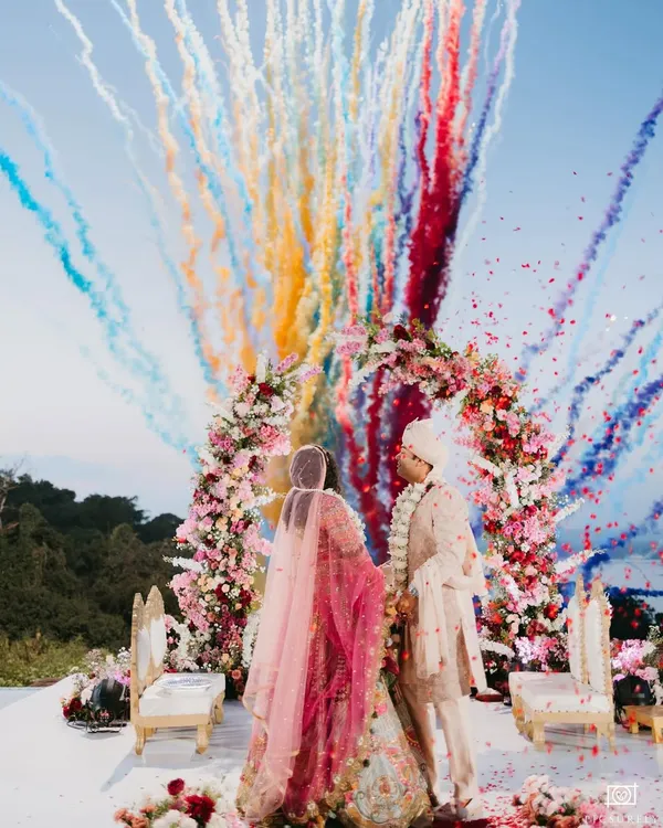 A spectacular varmala ceremony, framed by a floral arch and a burst of rainbow-colored smoke, perfectly captures the grandeur and joy of a destination wedding.