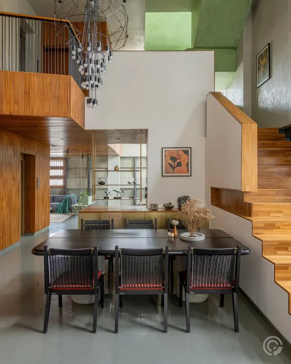 This double-height dining area is defined by a dramatic, contemporary chandelier and warm wood paneling. The space opens up to a mezzanine level, creating visual connection across different floors of the home.