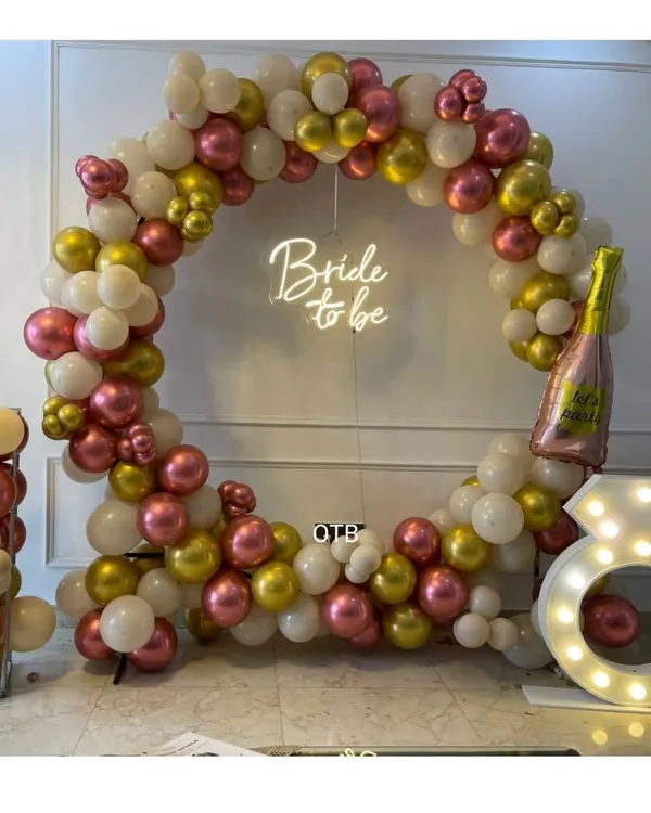 This is one of my most requested bridal shower designs. A full circular balloon arch in metallic pink, gold, and white, with a 'Bride to be' neon sign and a large light-up diamond ring prop.