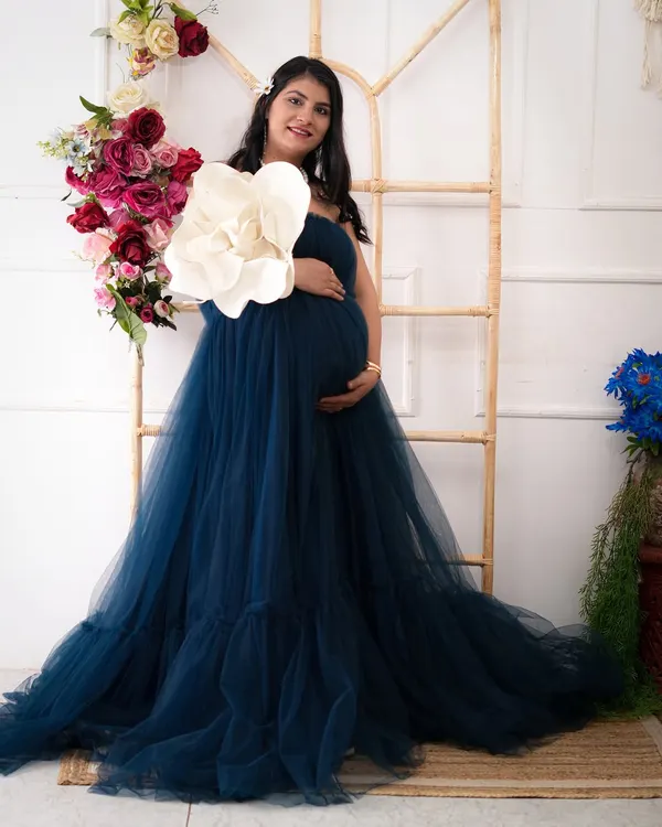 A solo portrait of the mother-to-be, radiating grace in a flowing teal gown. The floral arrangement and rustic ladder prop add a touch of elegance to this studio maternity session.