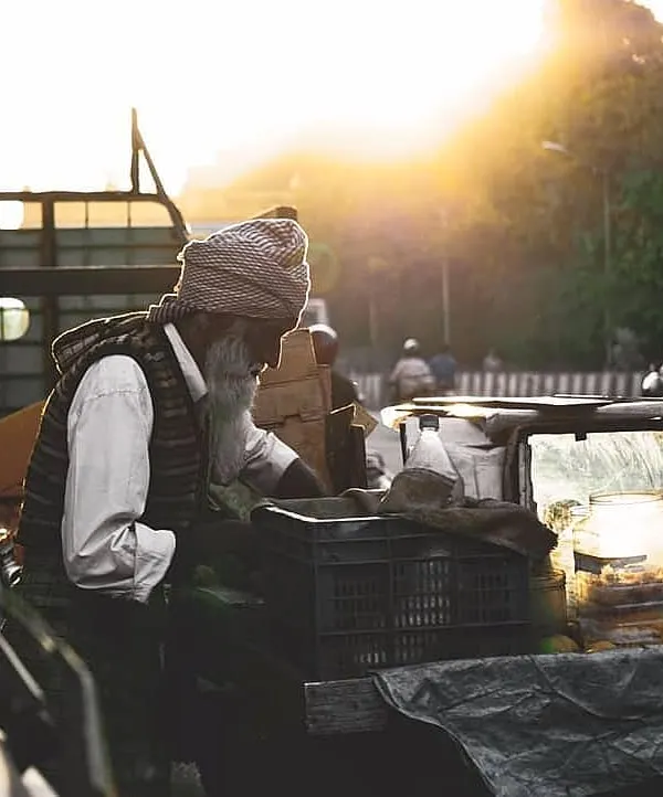 An elderly street vendor with a long white beard arranges his goods in the beautiful golden hour light. This candid street photograph captures a quiet moment of daily work in Bangalore.