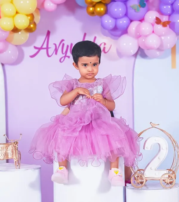 A sweet solo portrait of the birthday girl in her beautiful purple dress, set against the party's balloon decor.