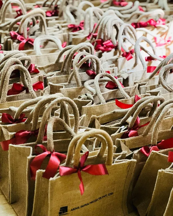 A large order of eco-friendly jute bags with rope handles and red ribbons, perfect for corporate event giveaways or welcome kits.